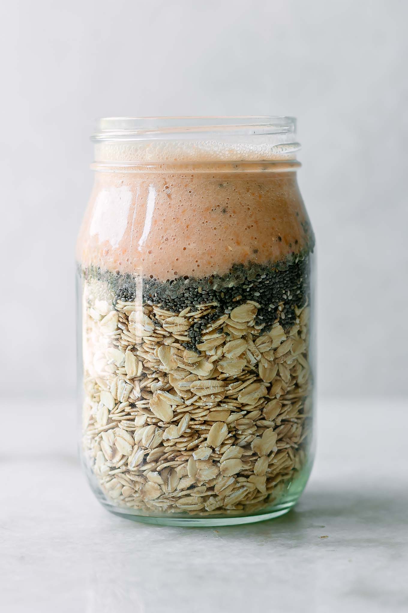 rolled oats, chia seeds, and apricot flavored milk in a mason jar on a white table