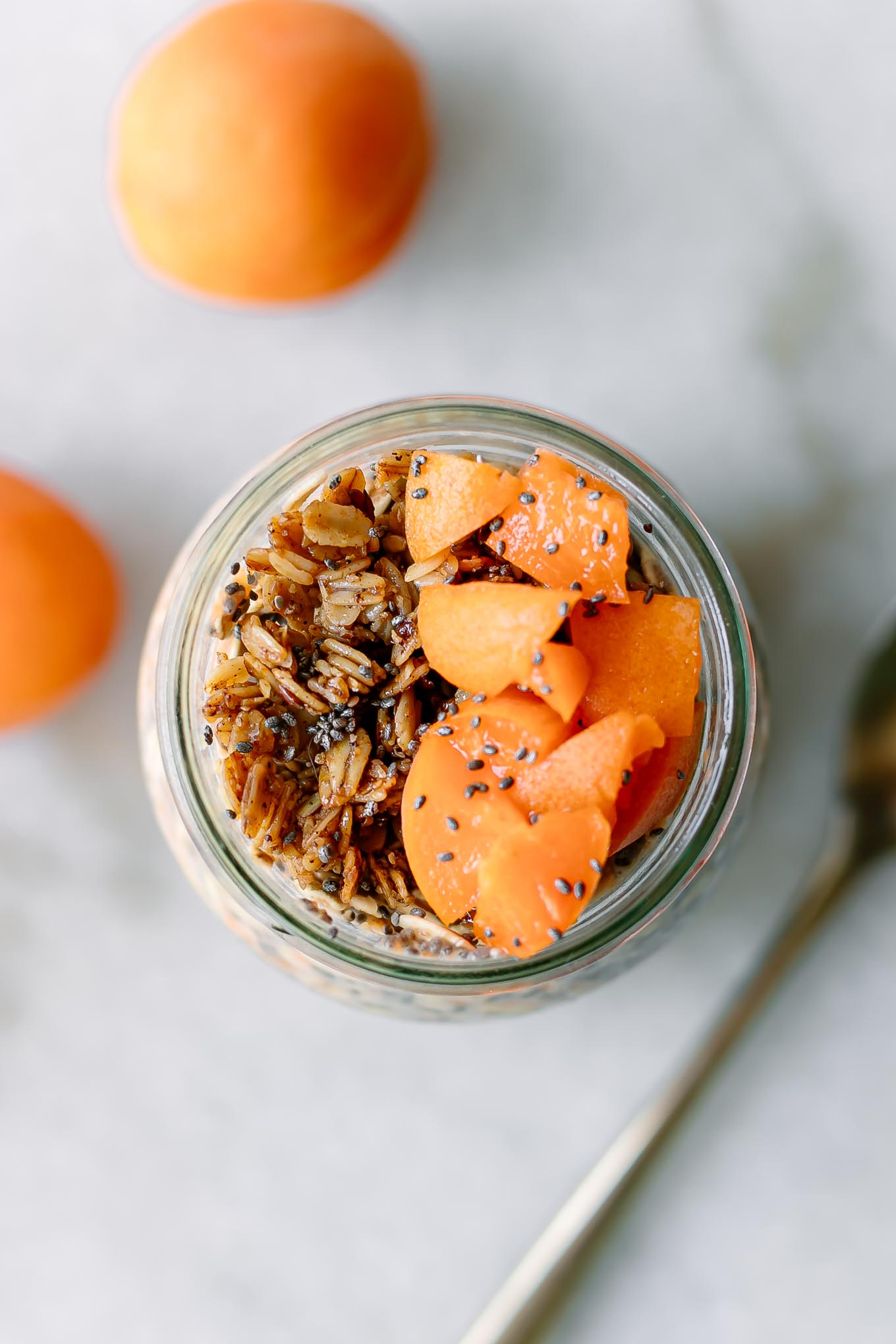 a close up photo of overnight oats with cut apricots and granola on a white table
