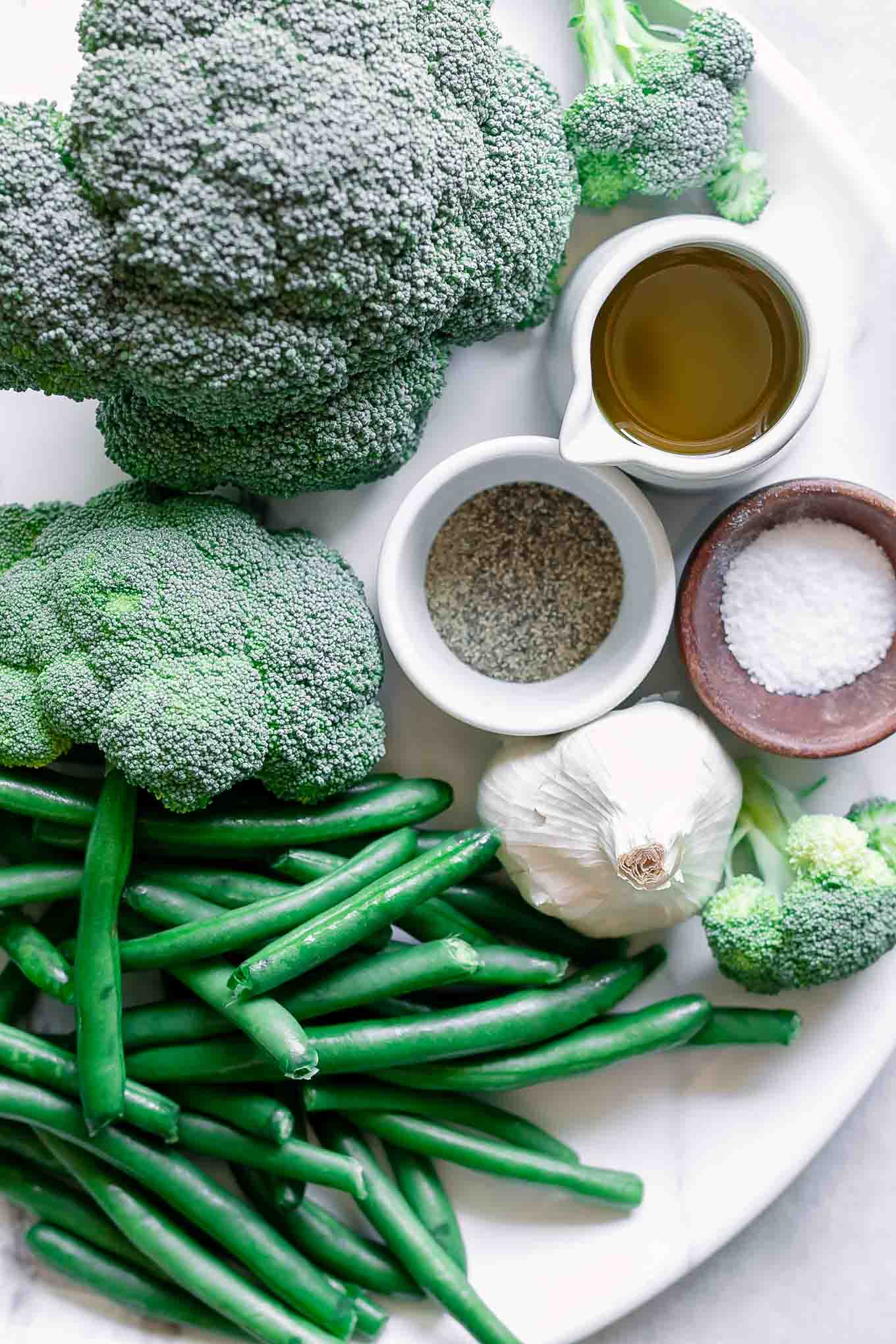 broccoli, green beans, garlic, and bowls of olive oil, salt, and pepper on a white table