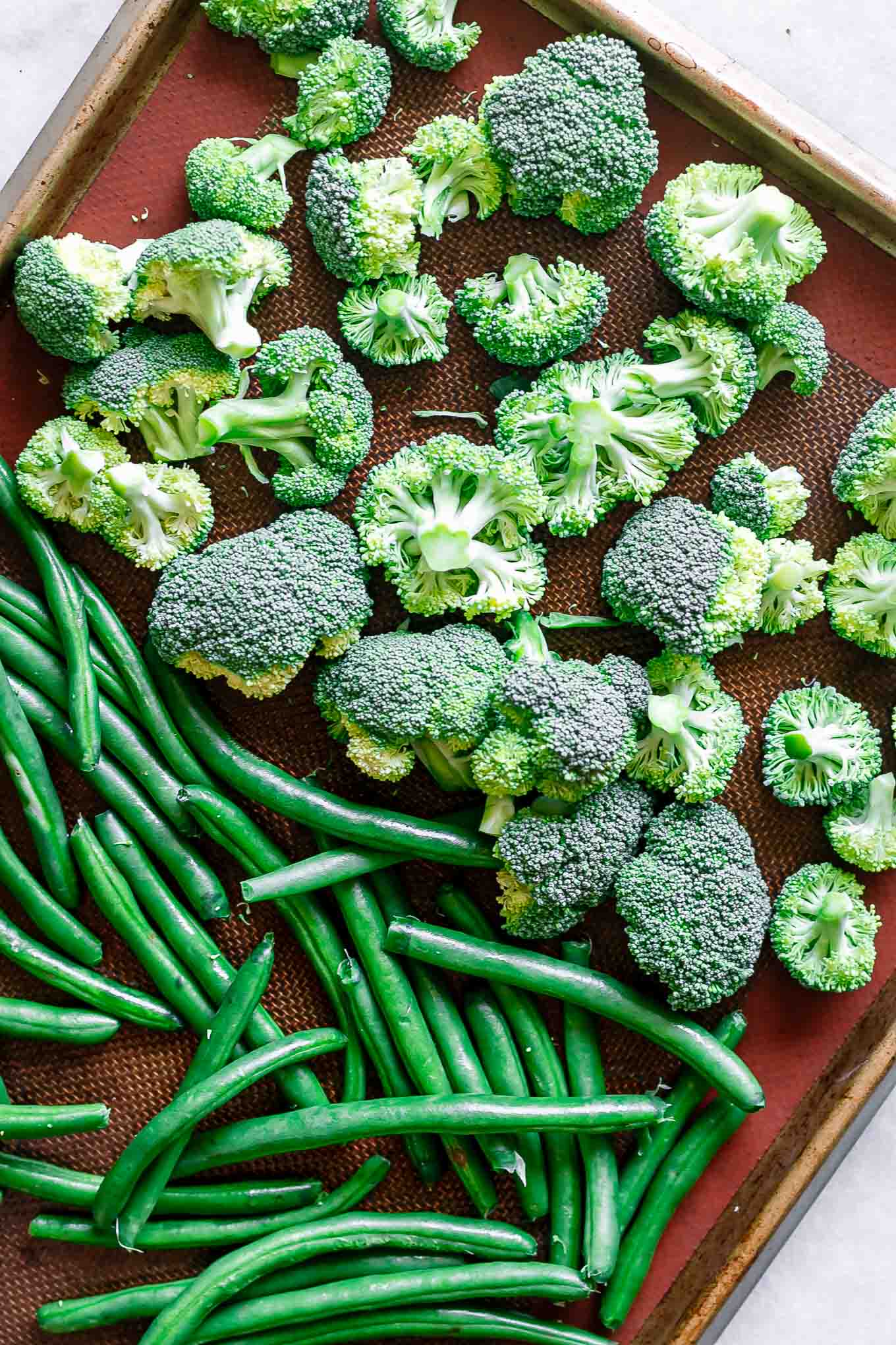 broccoli florets and green beans on a baking sheet before roasting