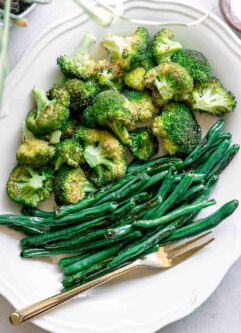 roasted green beans and broccoli on a white plate with a gold fork