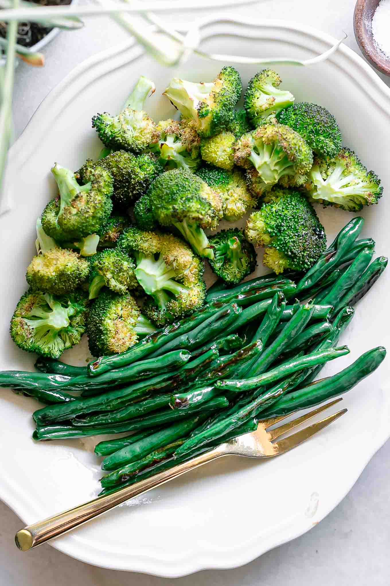 roasted green beans and broccoli on a white plate with a gold fork