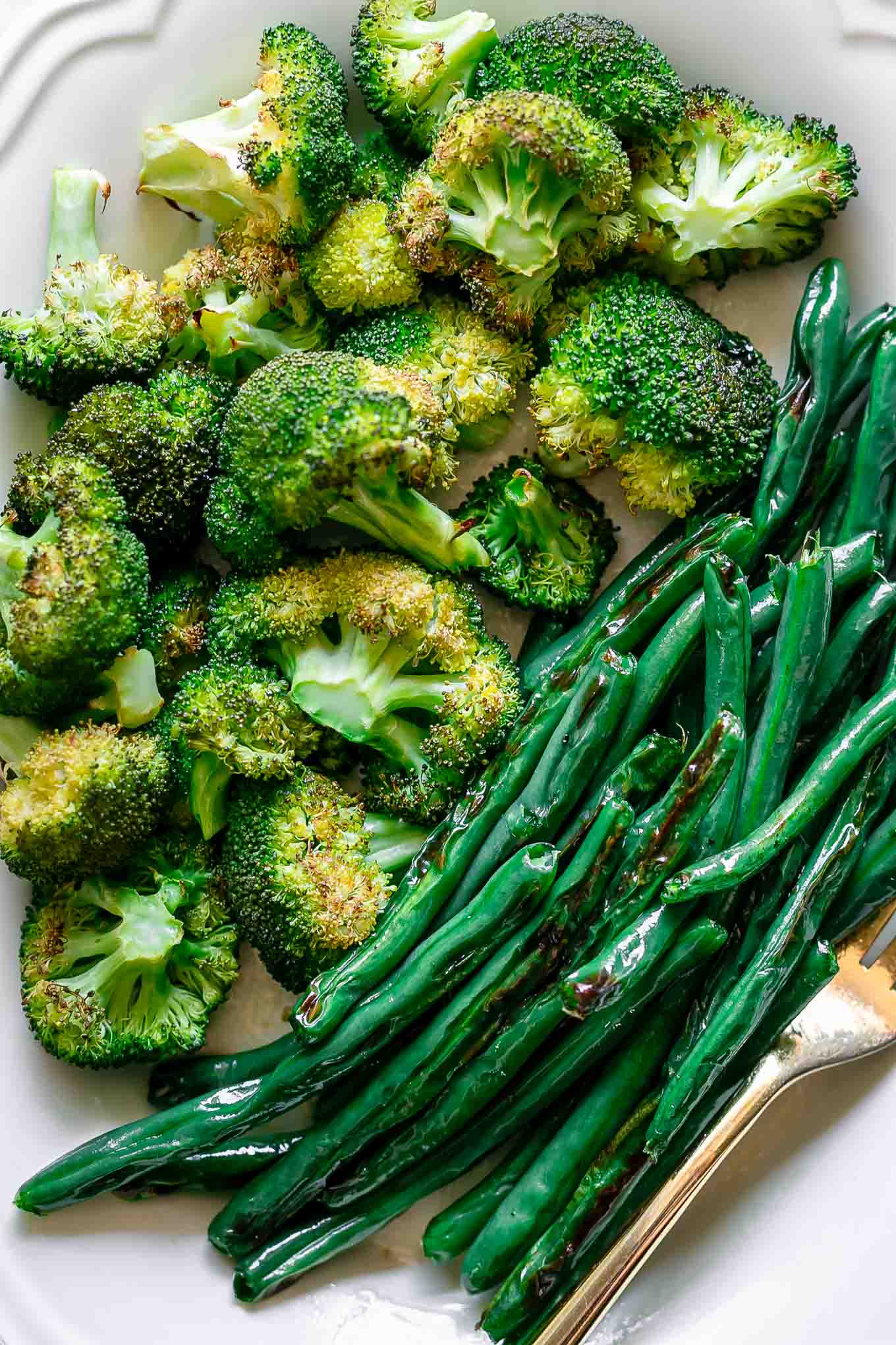 a close up photo of roasted green beans and broccoli on a white plate