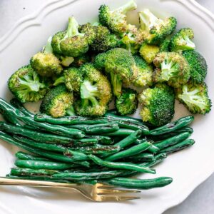 roasted broccoli and green beans on a white side dish with a gold fork on a white table