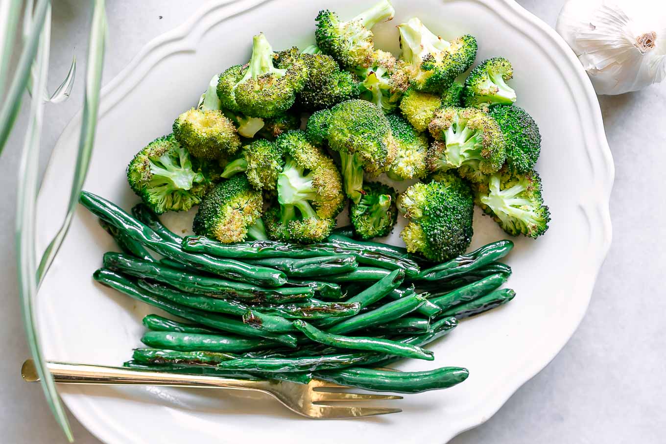 roasted broccoli and green beans on a white side dish with a gold fork on a white table
