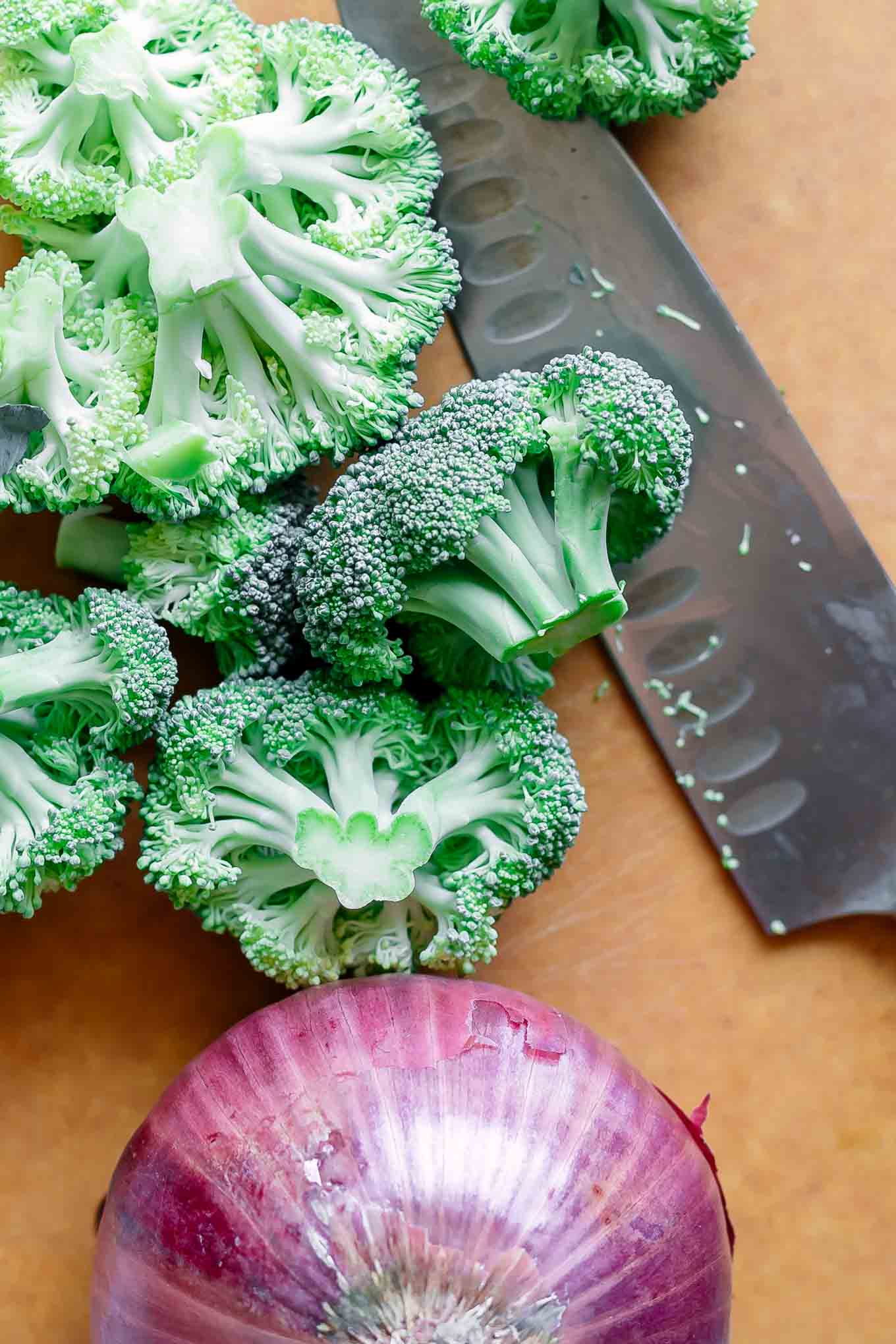 cut broccoli and onions on a cutting board before roasting