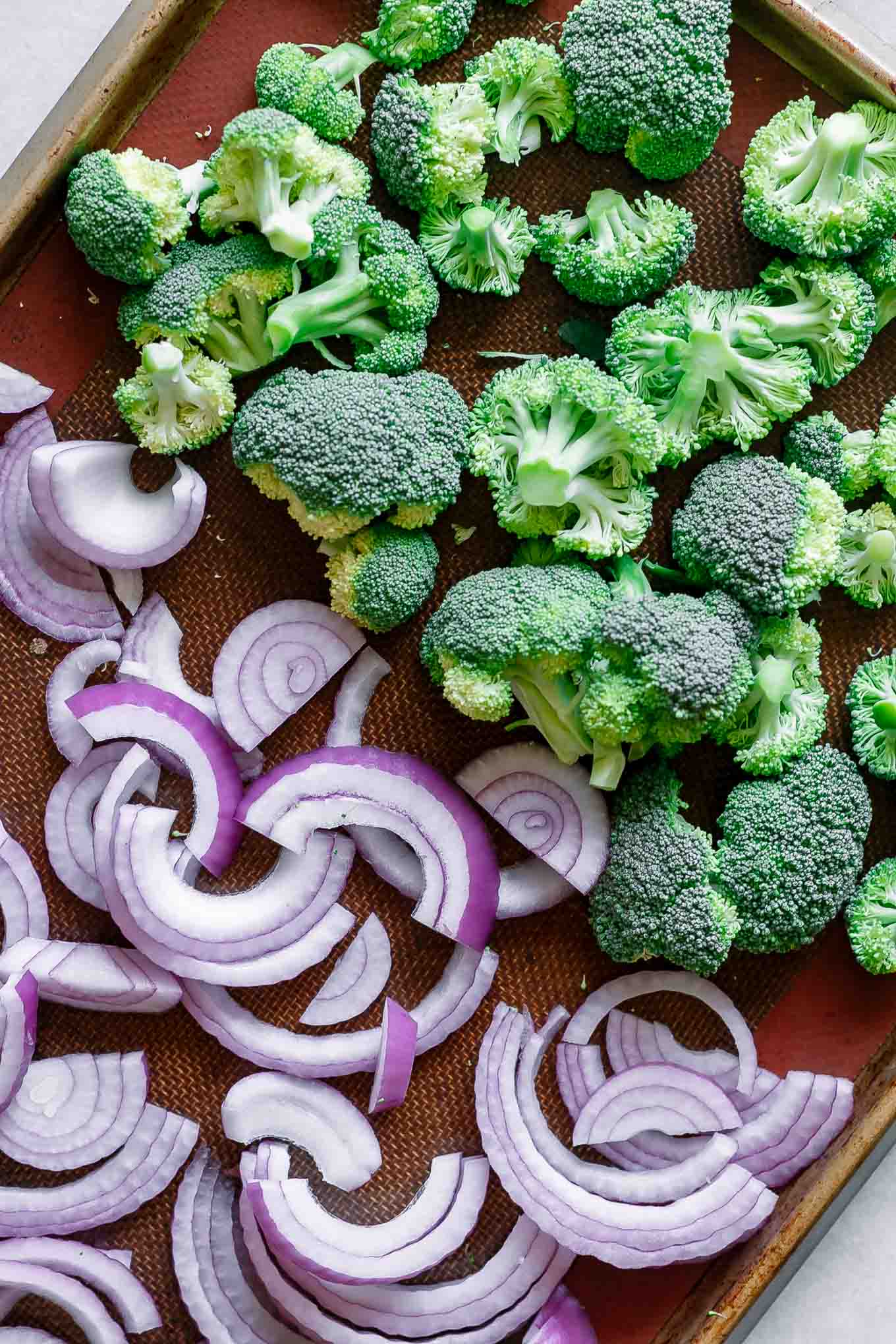 broccoli florets and onion slices on a baking sheet before roasting