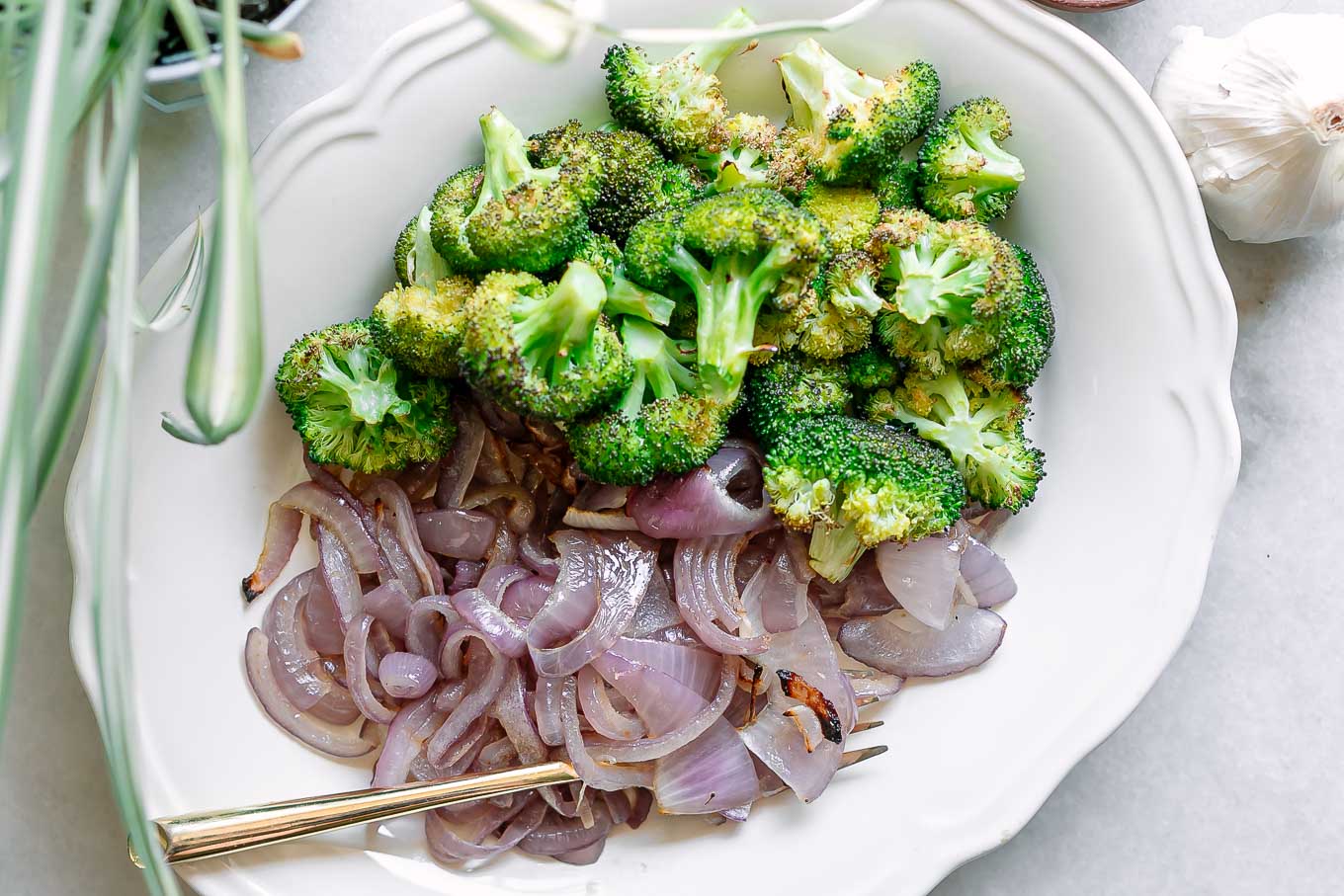 roasted broccoli and onions on a white side dish with a gold fork on a white table