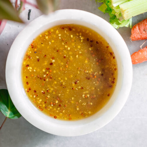 maple dijon salad dressing in a white bowl on a white table with vegetables