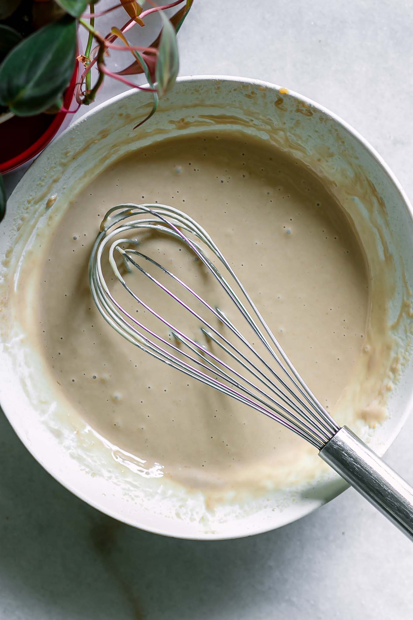 a bowl with tahini and miso dressing mixed with a whisk on a white table