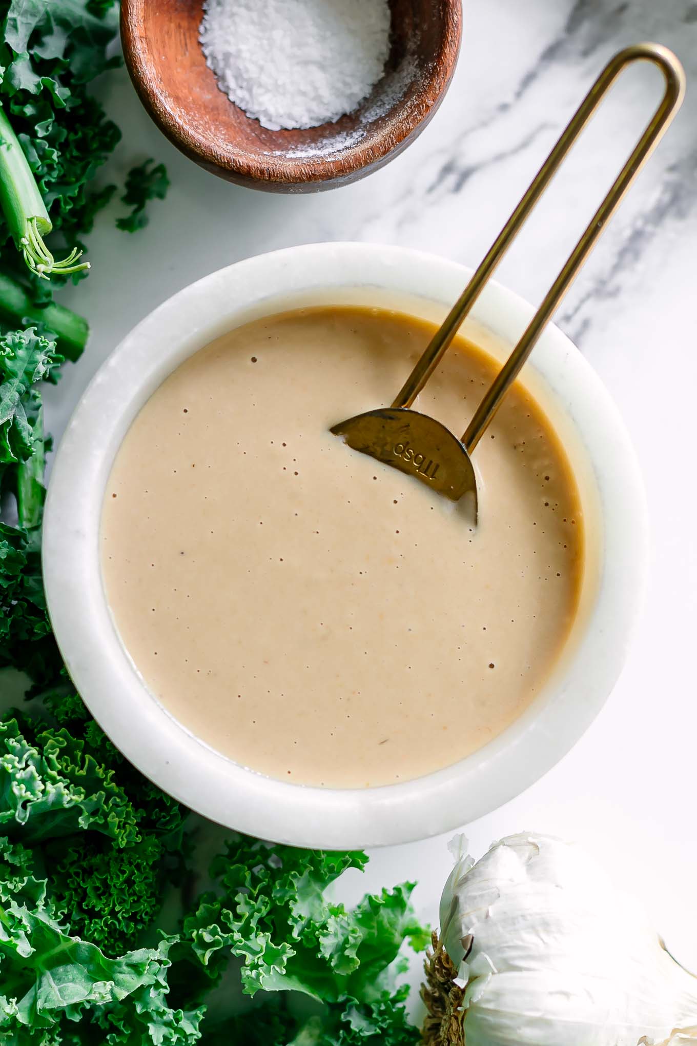 a white bowl with creamy miso tahini dressing with a gold spoon on a white table