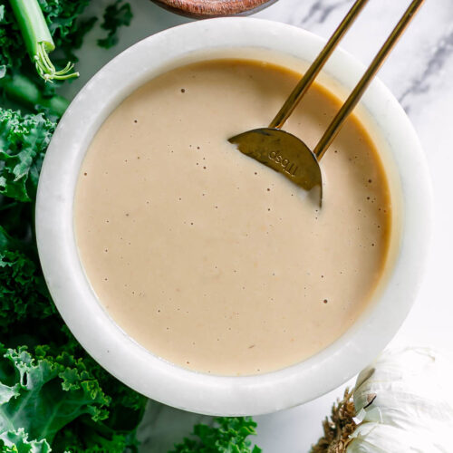 a miso tahini dressing in a white bowl on a white table with a gold spoon
