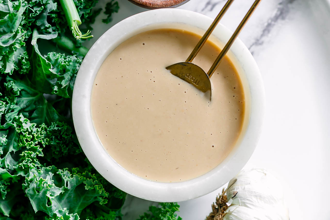 a miso tahini dressing in a white bowl on a white table with a gold spoon