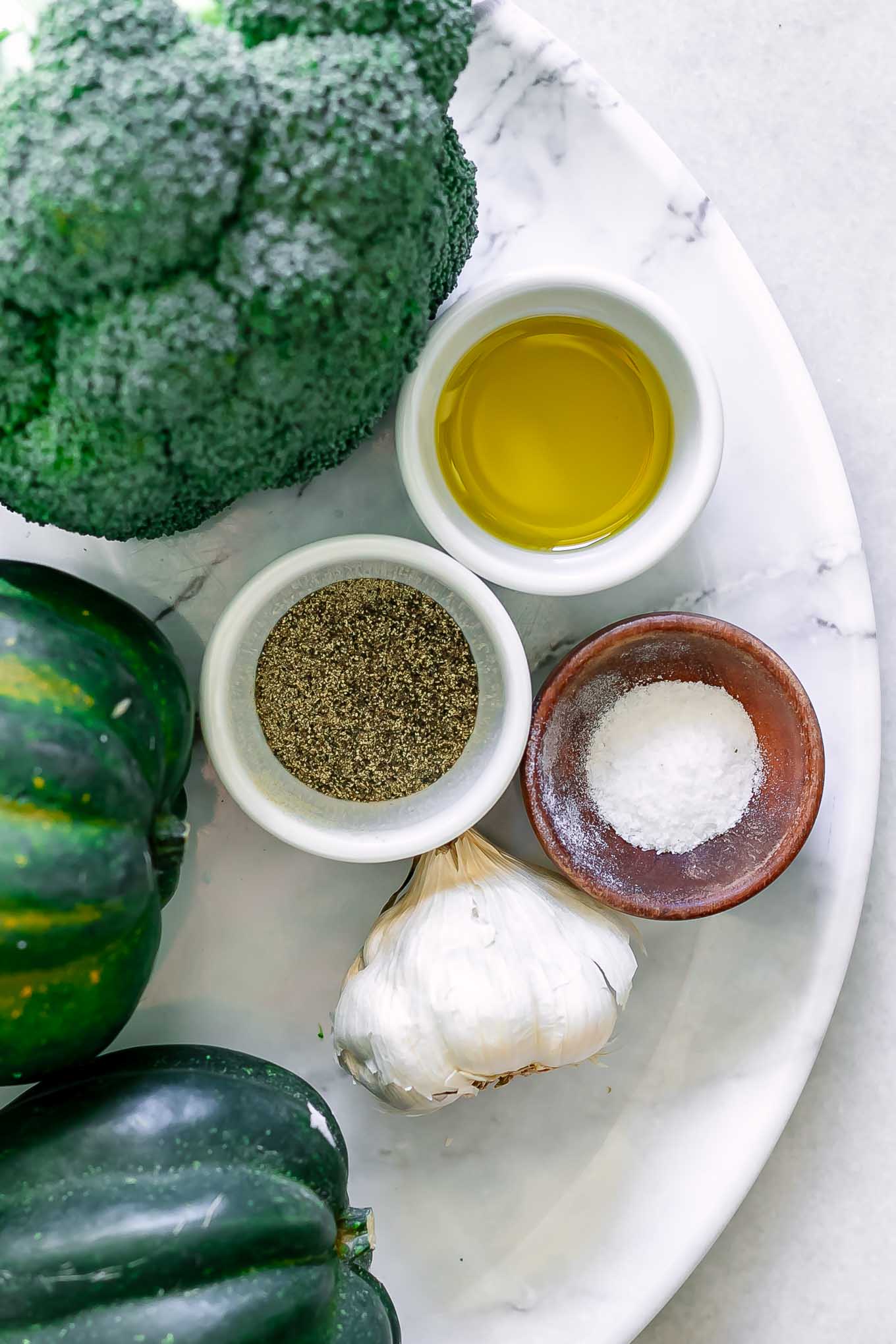 broccoli florets and acorn squash on a white table with oil, garlic, salt, and pepper before roasting