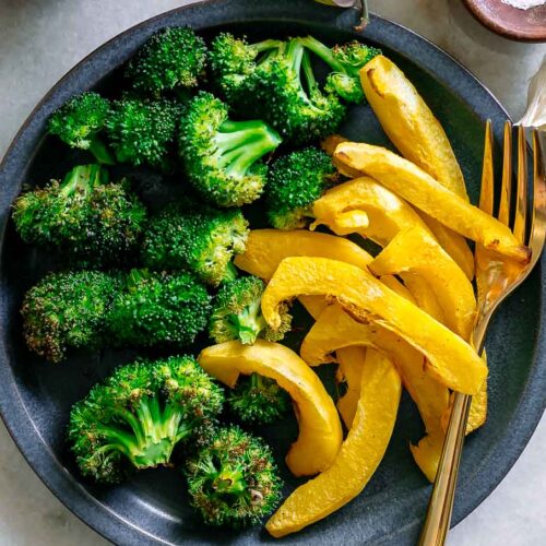 roasted broccoli and acorn squash on a blue dish on a white table with a gold fork