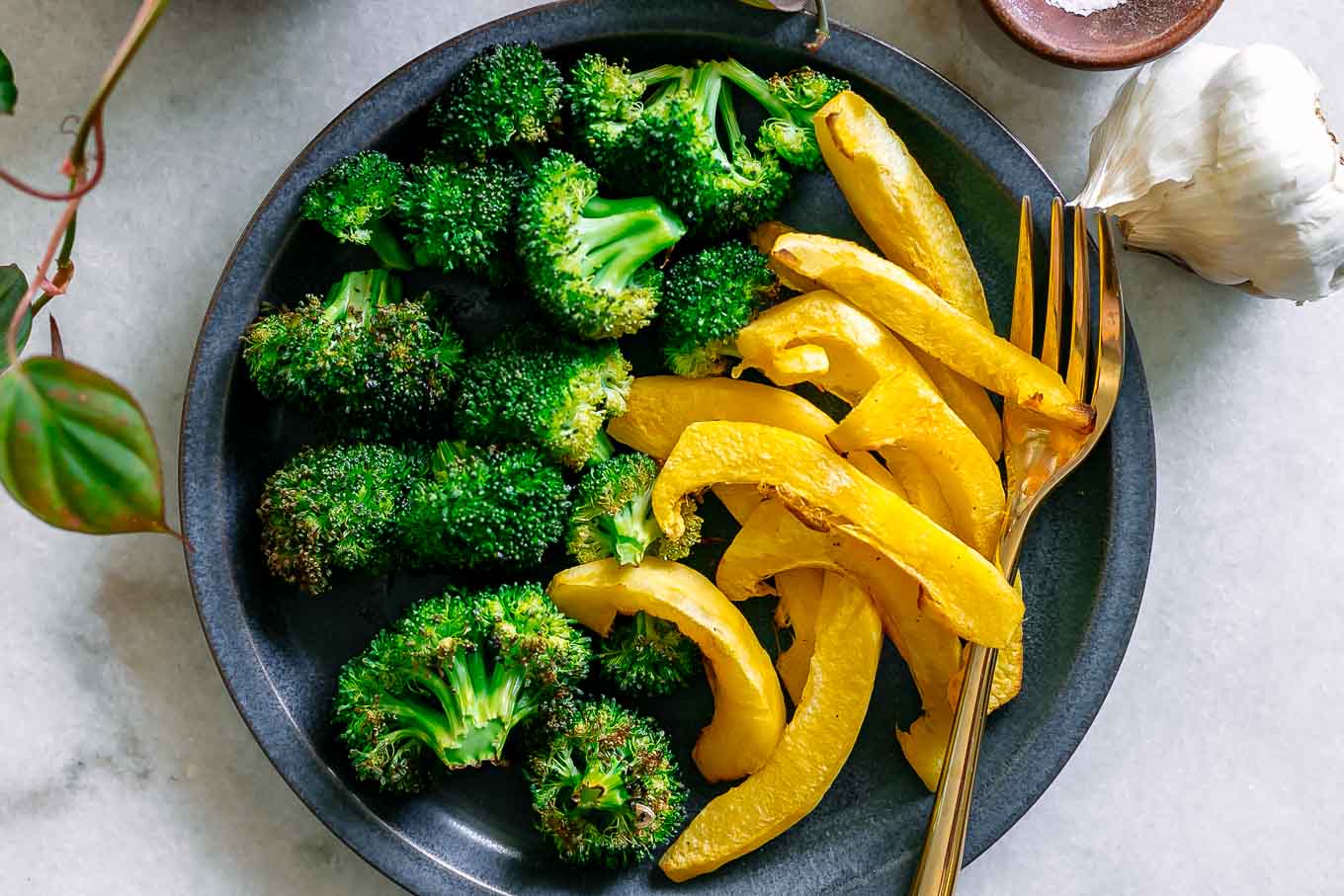 roasted broccoli and acorn squash on a blue dish on a white table with a gold fork