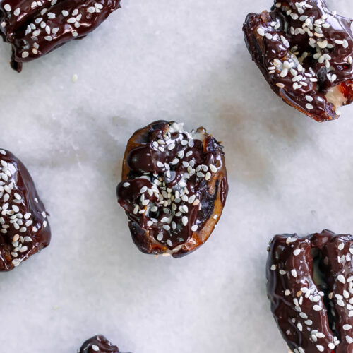 tahini stuffed dates coated with chocolate and sprinkled with sesame seeds on a white table