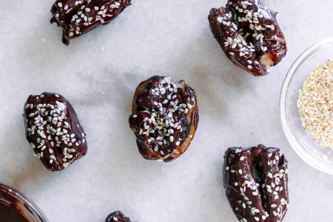 tahini stuffed dates coated with chocolate and sprinkled with sesame seeds on a white table