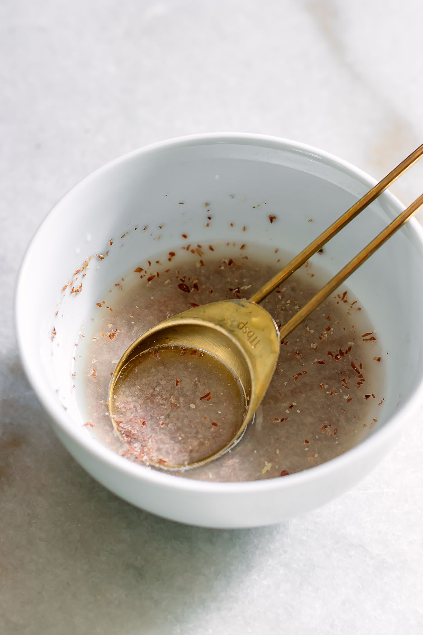 a flax egg made with ground flax seed and water in a white bowl with a gold spoon