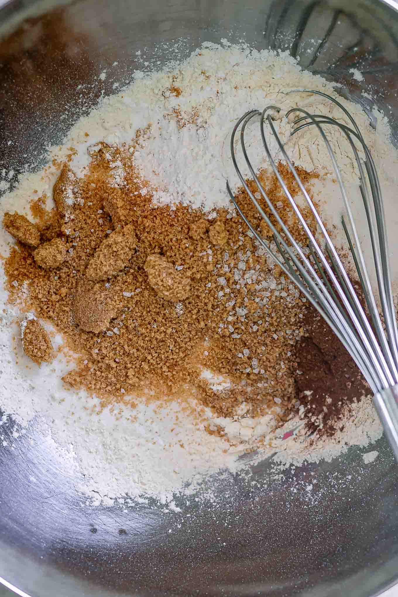 a mixing bowl with dry ingredients for bread, including flour, sugar, salt, baking soda, baking powder, and whisk