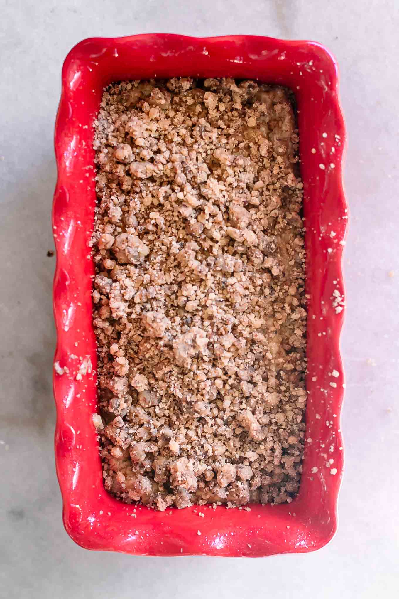 a red bread loaf pan with zucchini bread batter and a crumb topping before baking