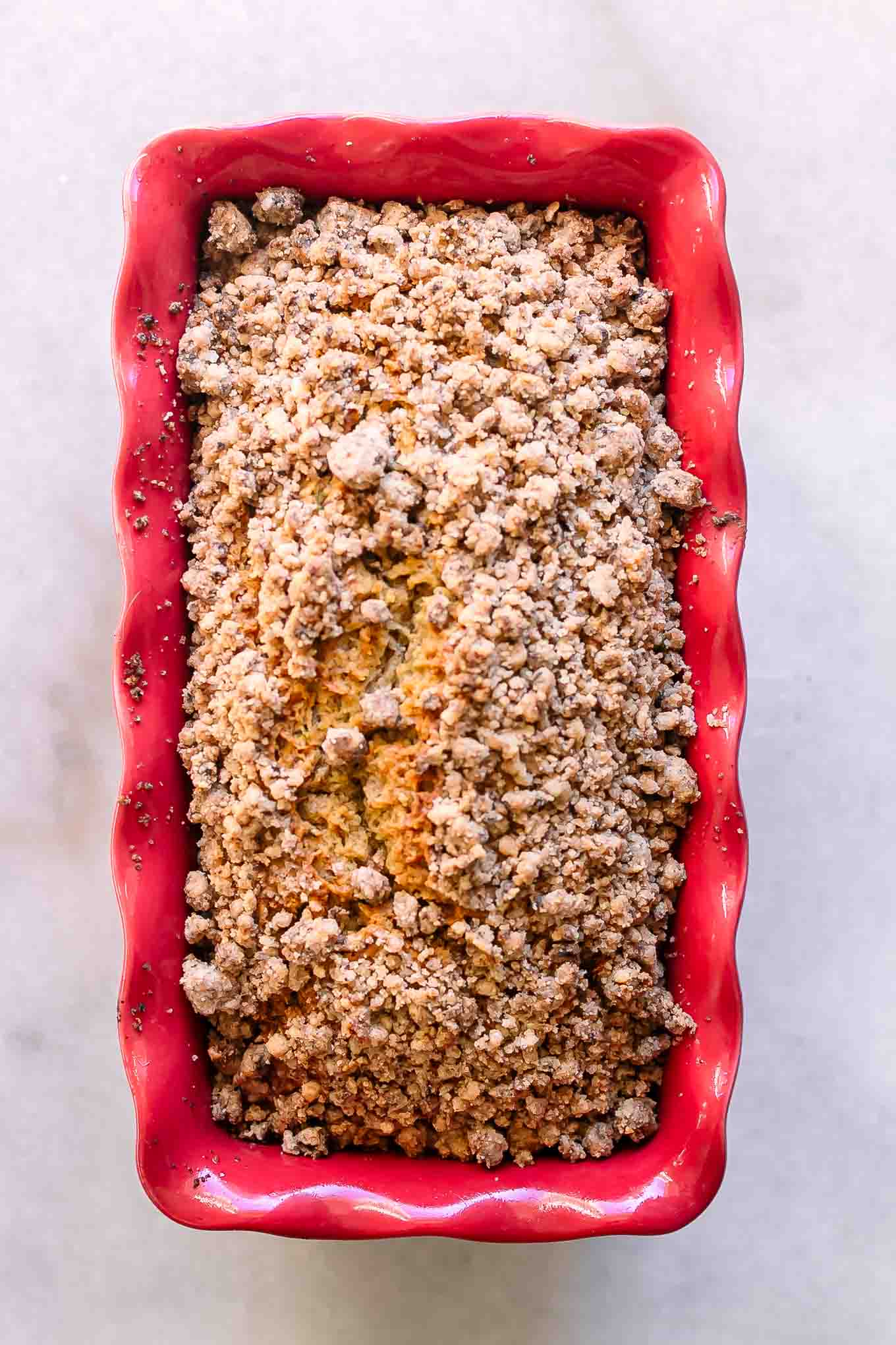 baked zucchini bread with a crumb topping in a red bread pan on a white table