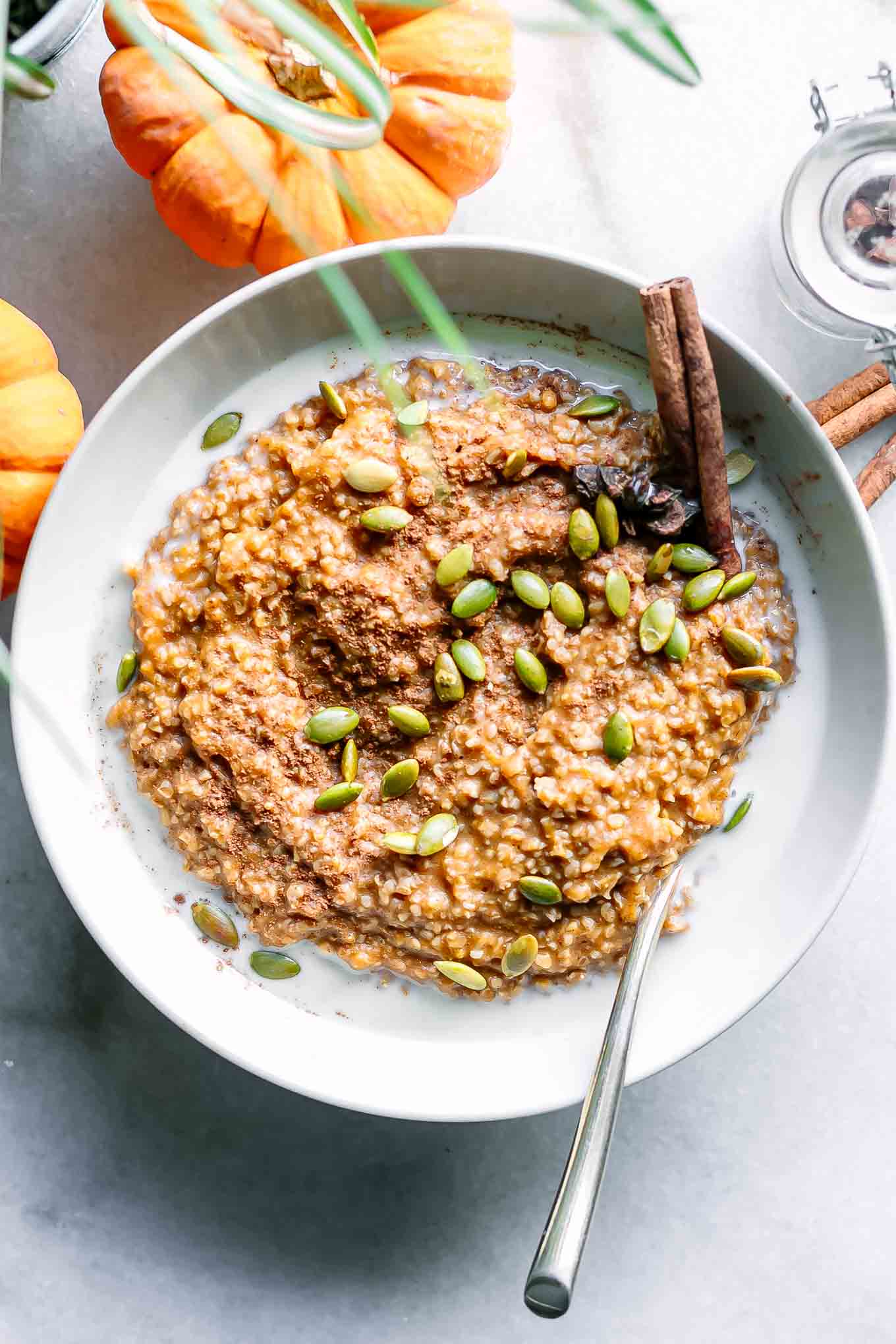 a bowl of oatmeal with pumpkin and pumpkin seeds on a white table with mini pumpkins