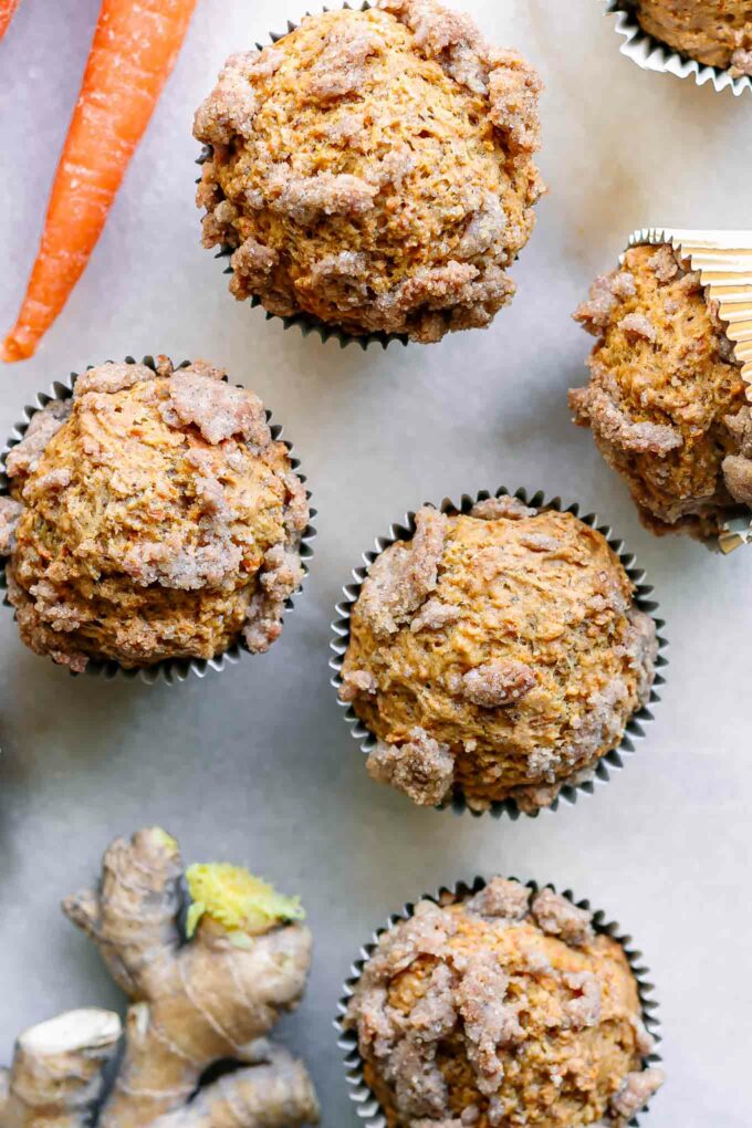 vegan carrot cake muffins on a white table with carrots and fresh ginger