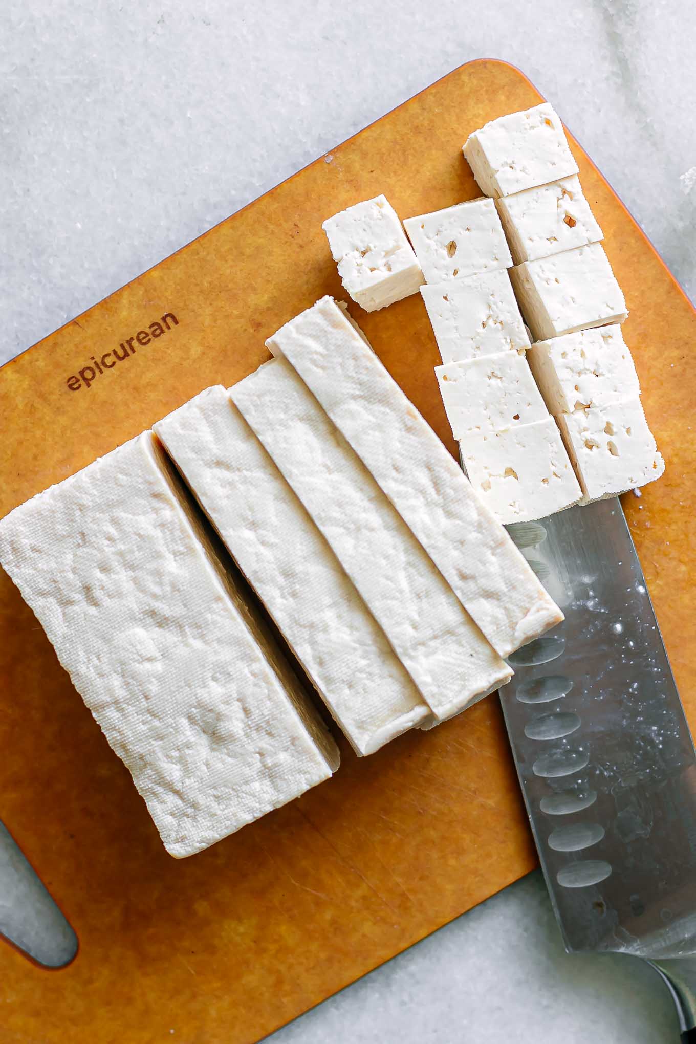 tofu on a cutting board with a knife cut into squares
