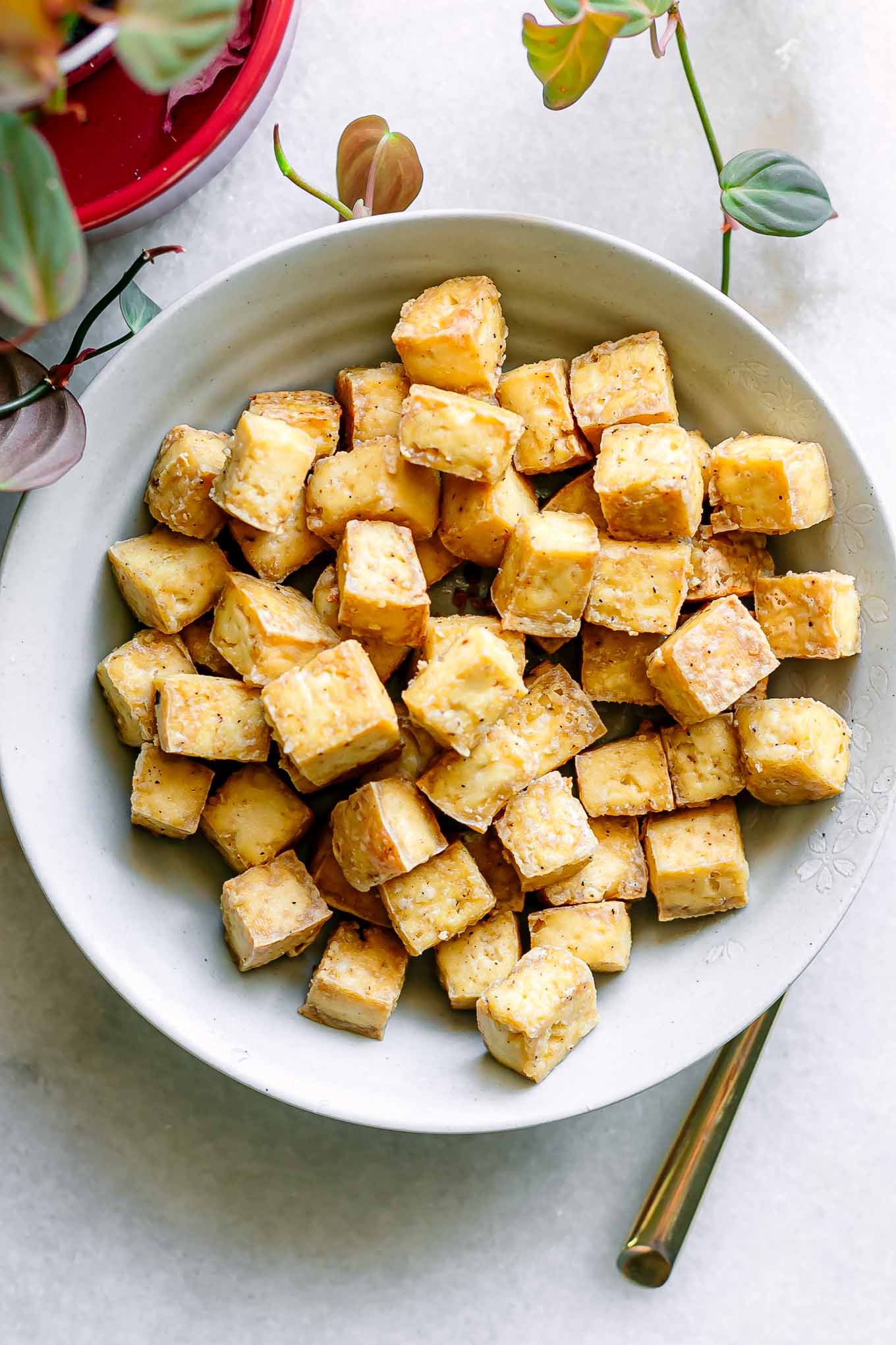 a bowl with crispy tofu on a white table with a gold fork