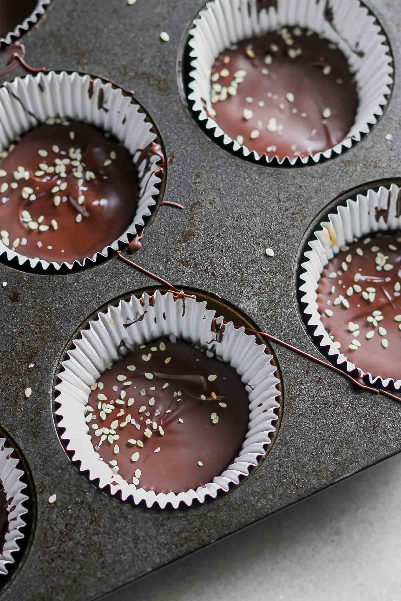 homemade chocolate cups garnished with sesame seeds inside a muffin liner