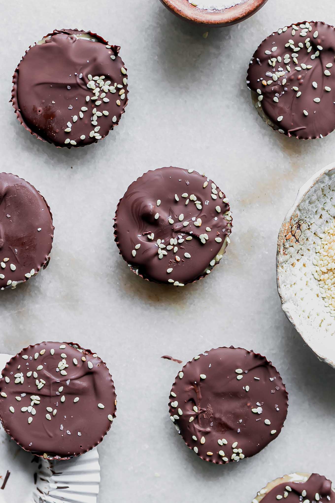 dark chocolate cups filled with tahini and garnished with sesame seeds on a white marble table