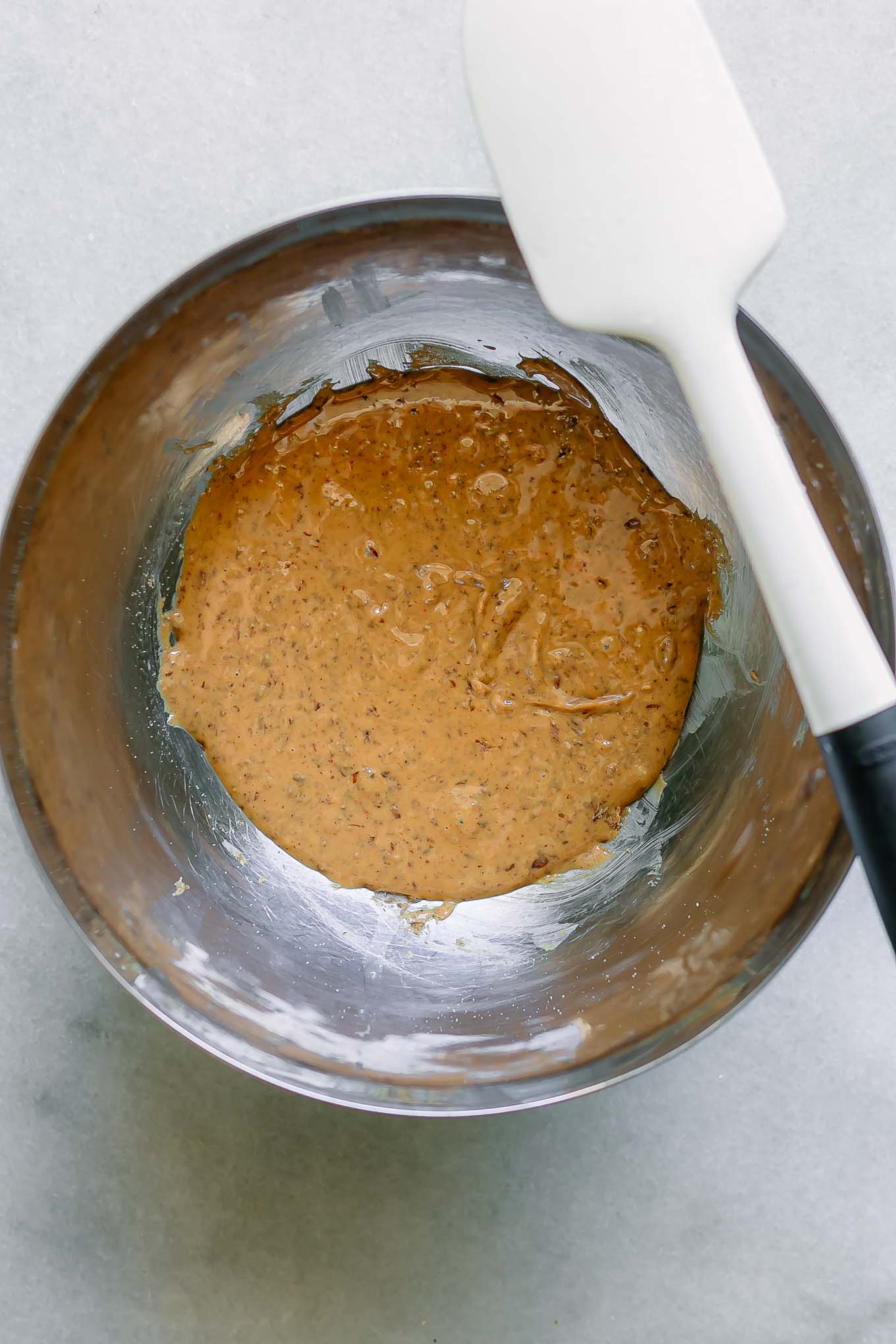 a metal bowl with peanut butter mixed with ground flaxseed on a white table