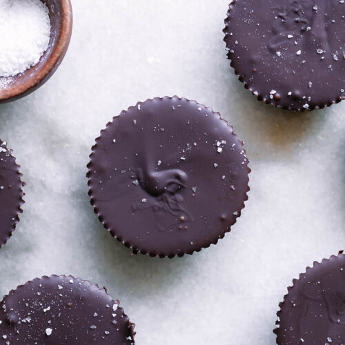 dark chocolate peanut butter cups on a white table with a bowl of sea salt for garnish