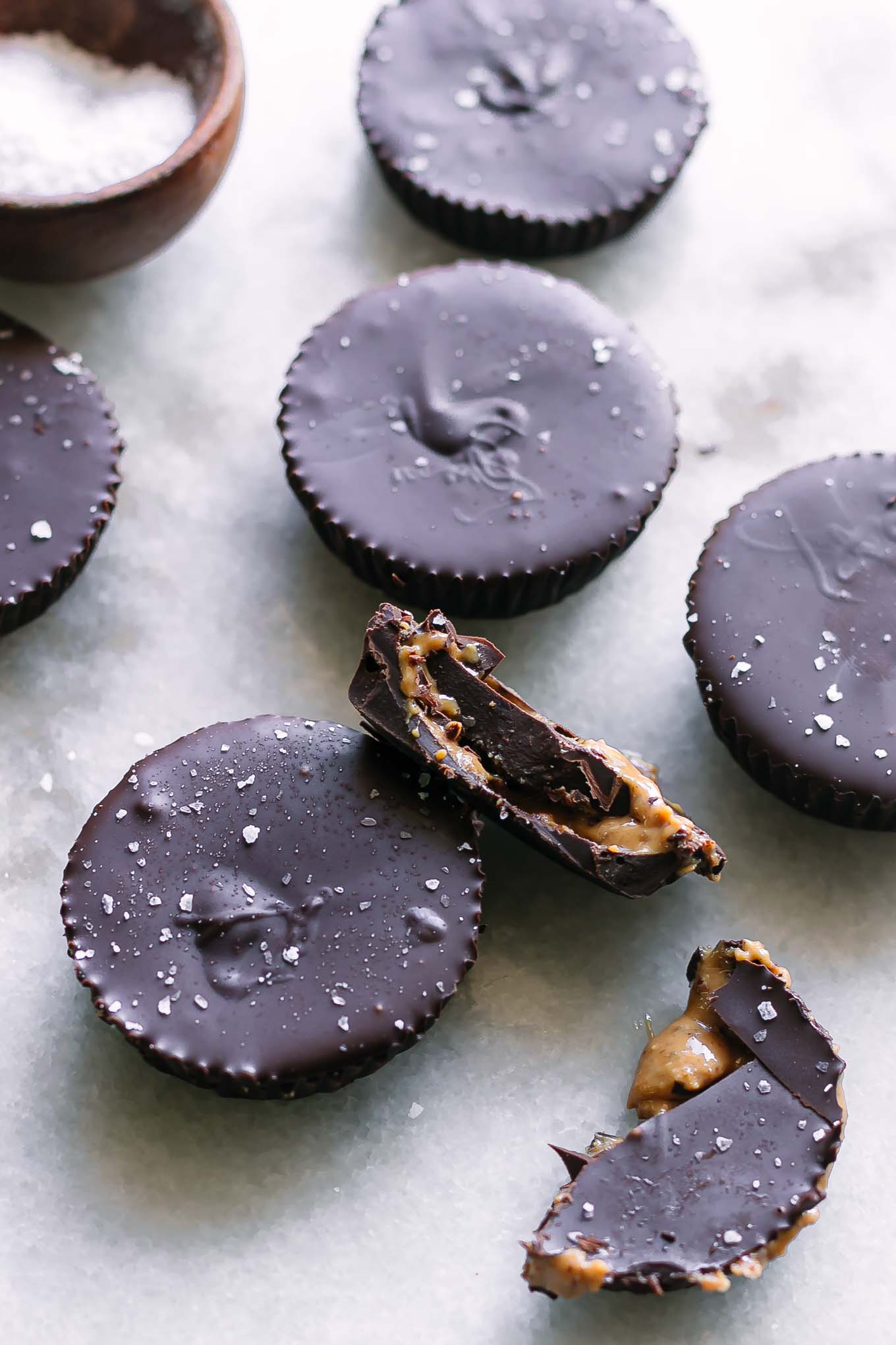 homemade chocolate peanut butter cups on a white table with one cut in half with peanut butter coming out