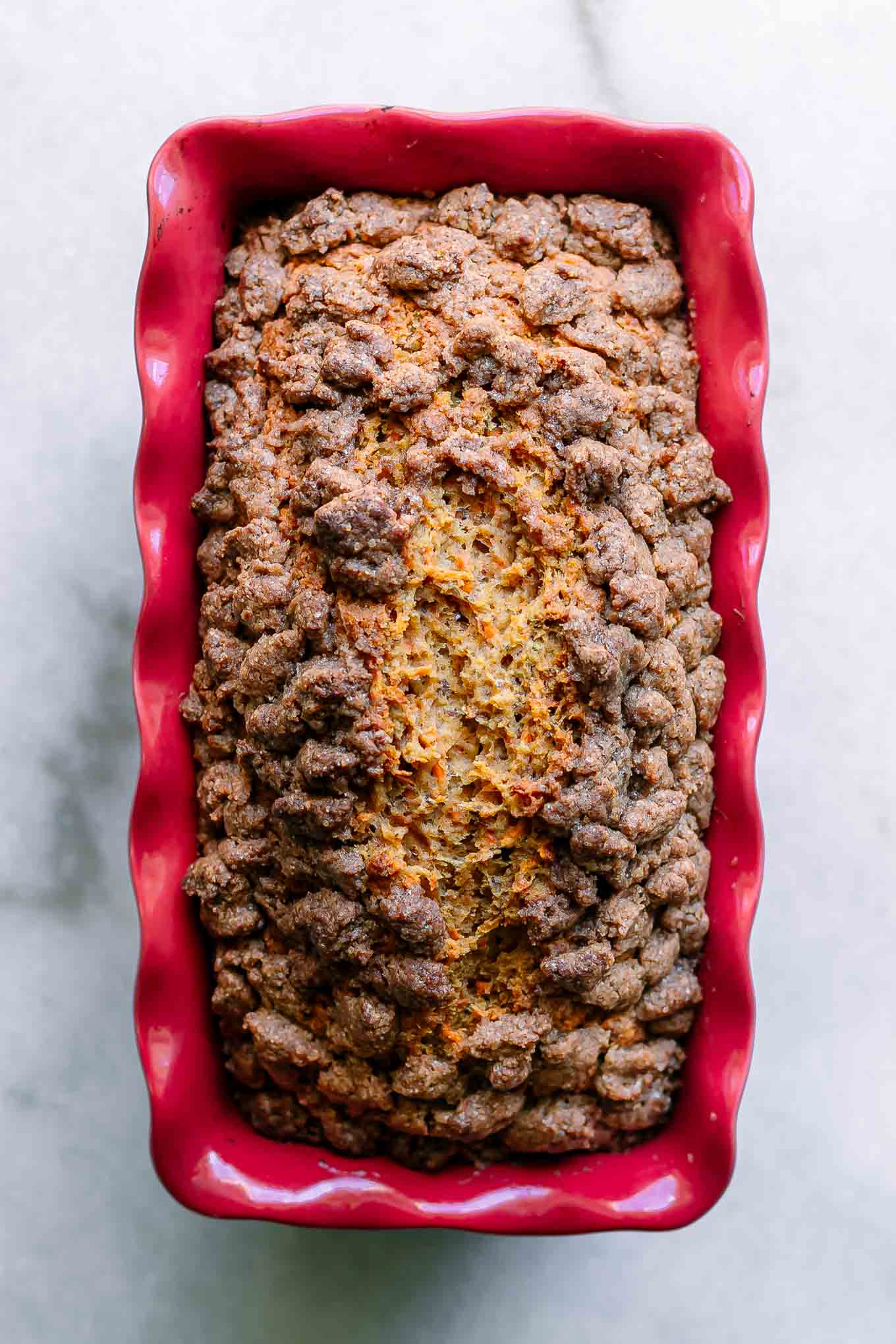 carrot cake bread in a red baking dish cooling on a white table
