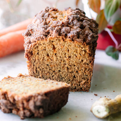 a sliced loaf of carrot cake bread on a table with fresh ginger and carrot