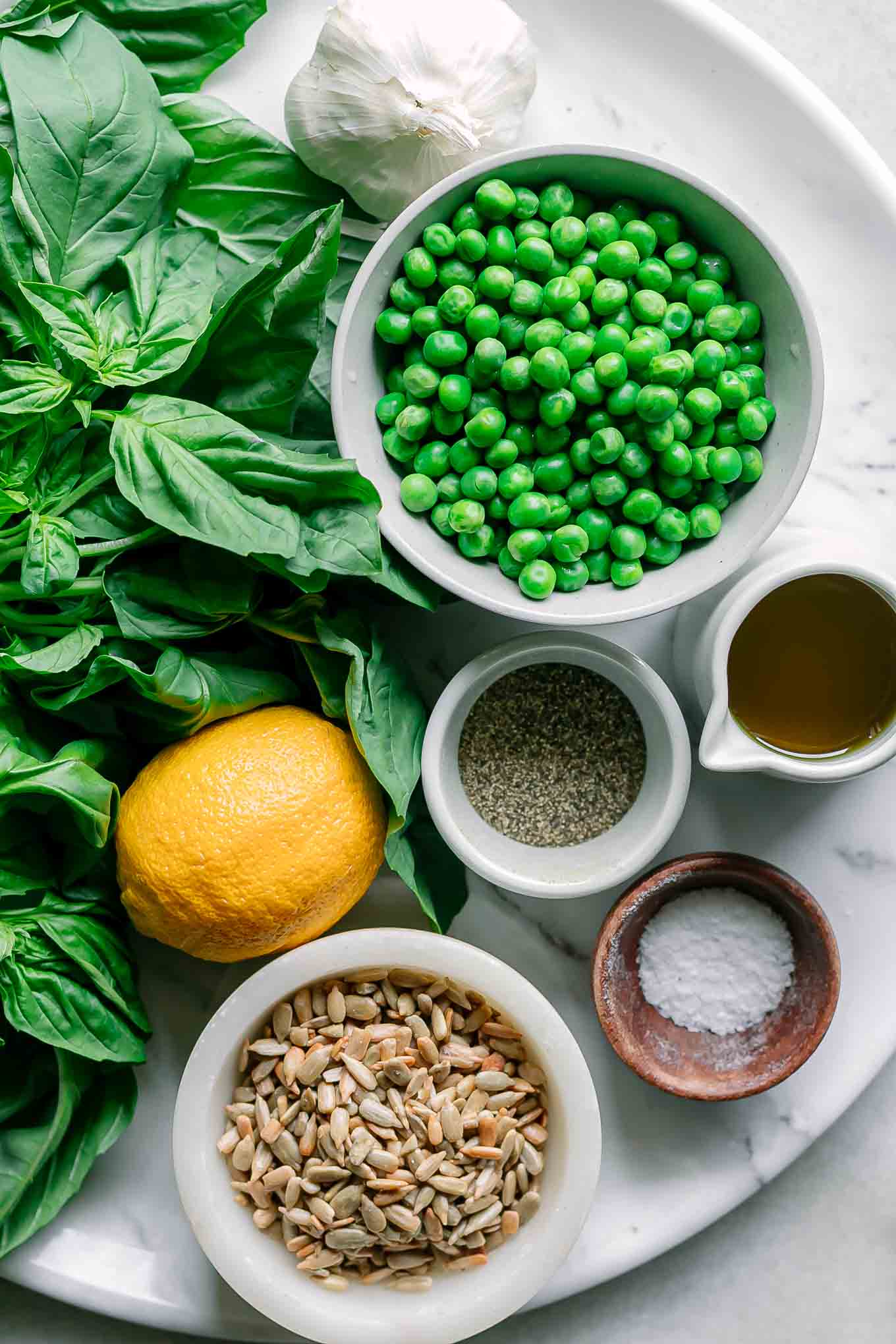 bowls of peas, nuts, oil, spices, and basil for pea pesto