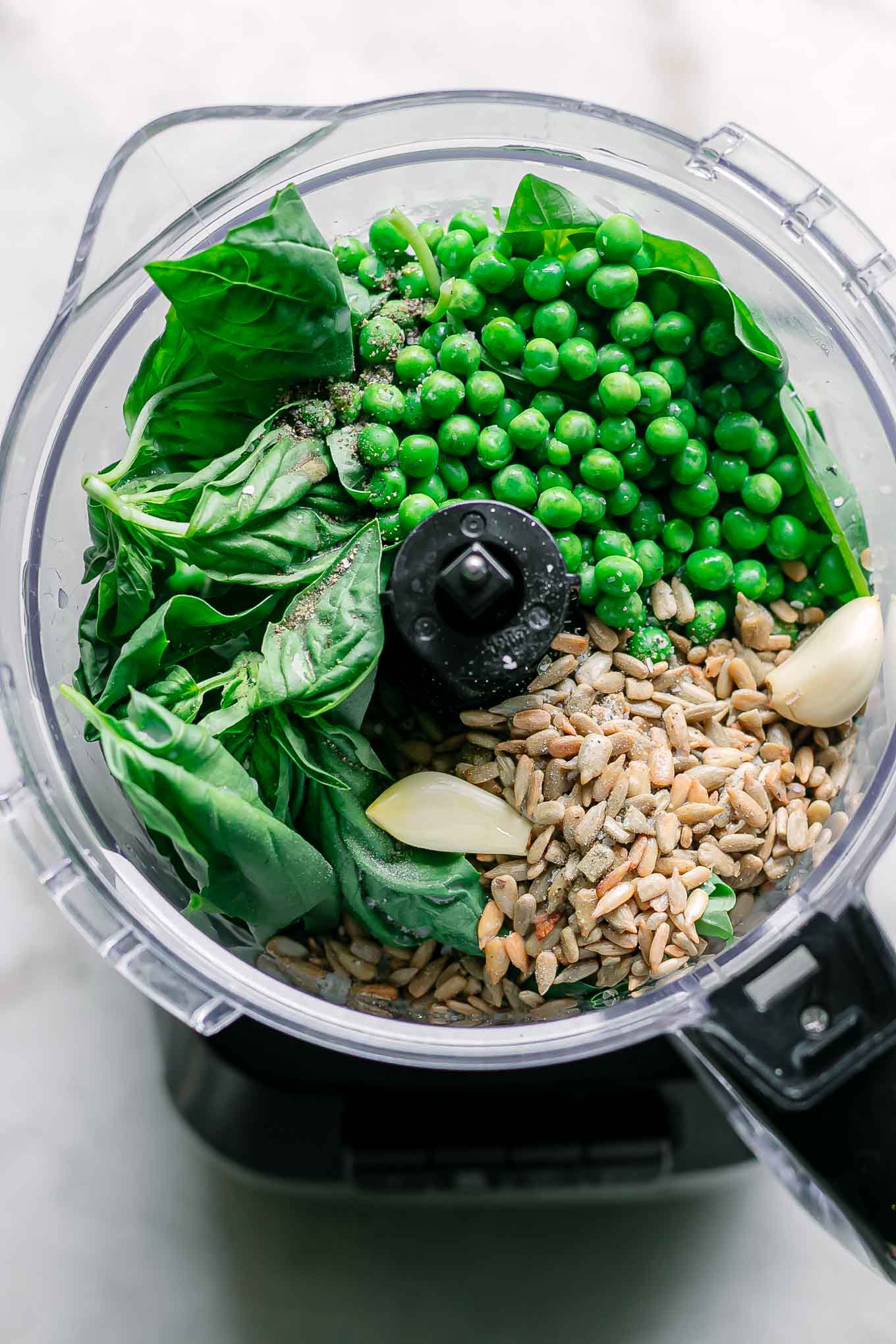 peas, basil, nuts, garlic, and other ingredients for pesto inside a food processor before blending