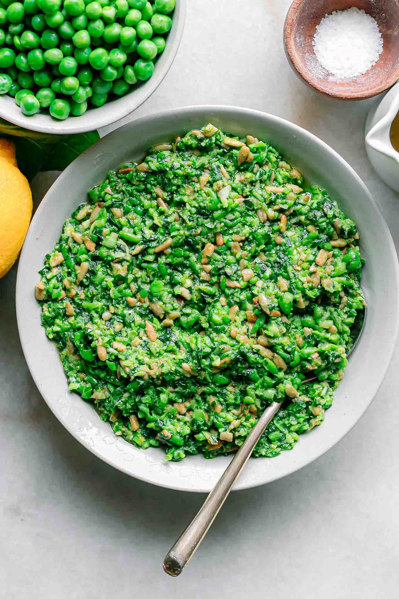 green pea pesto in a white bowl with a gold fork on a white table