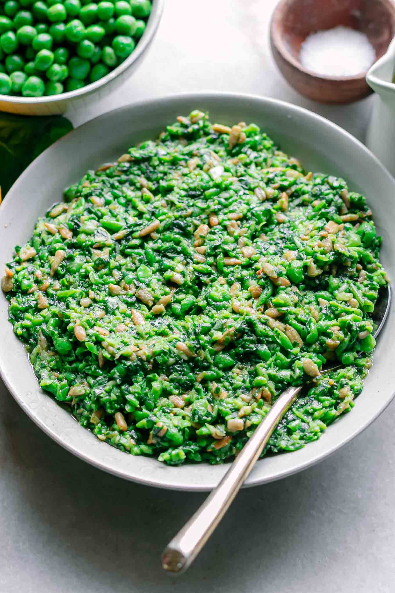 a bowl of spring pea pesto on a white table with a gold spoon
