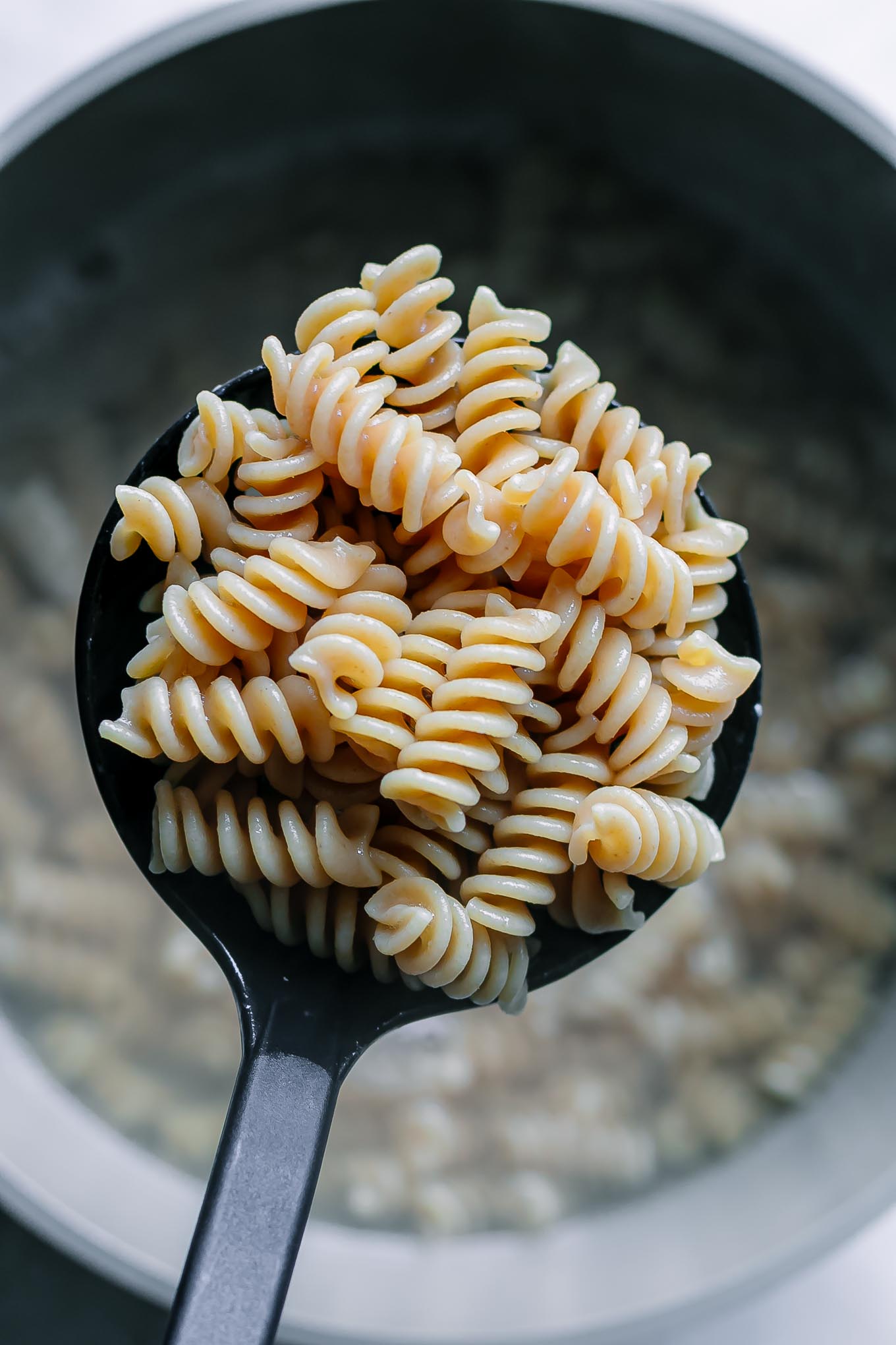cooked rotini pasta on a spoon over a pot of boiling water