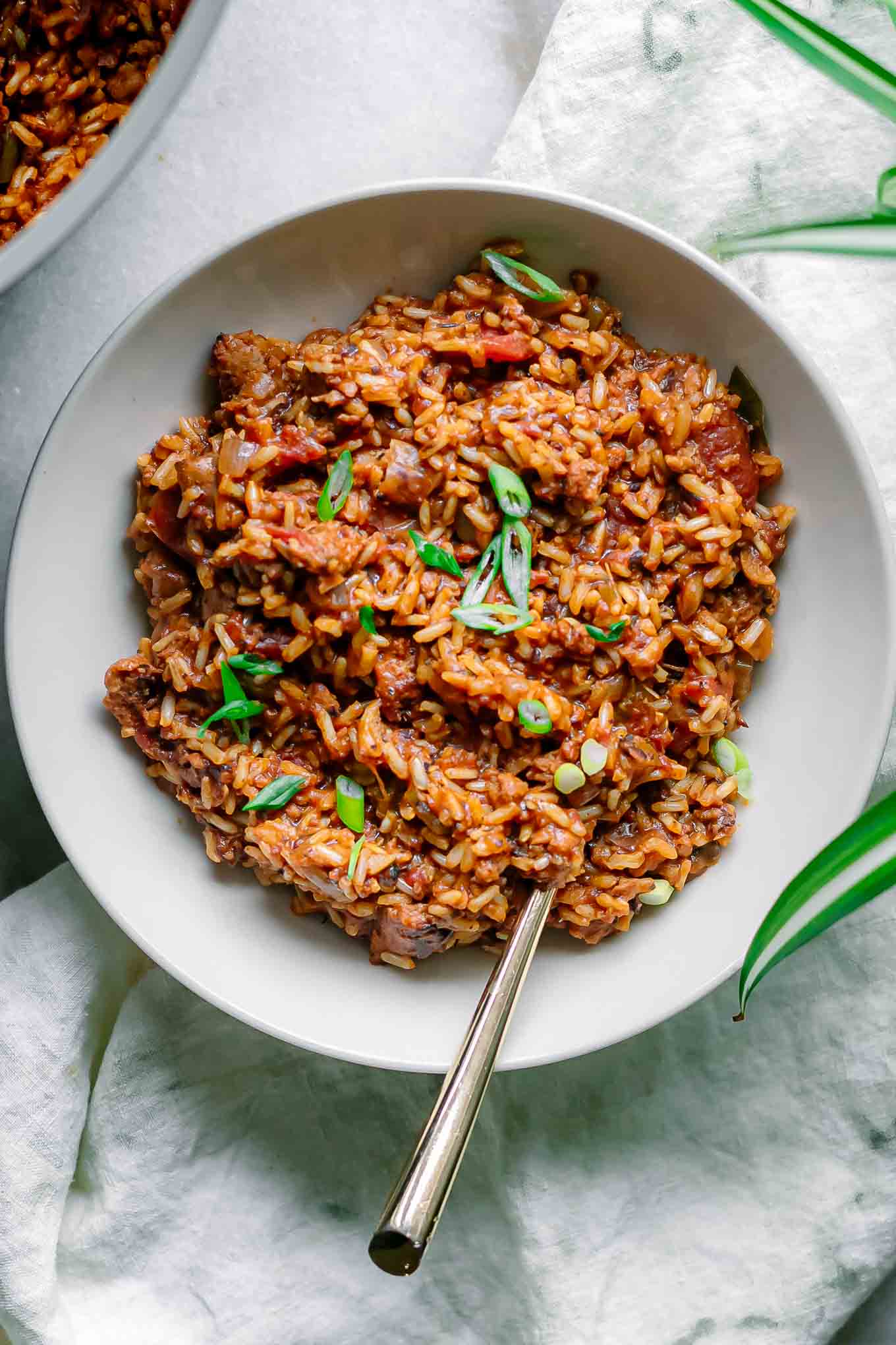 vegan jambalaya rice in a white bowl with a gold fork on white table