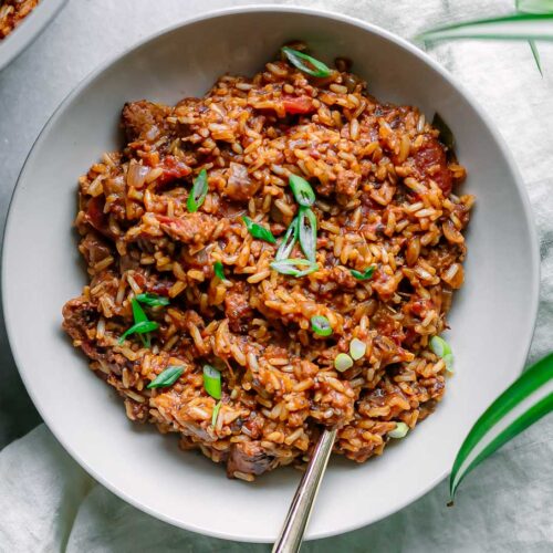 a bowl of vegan jambalaya on a white table garnishes with green onion slices