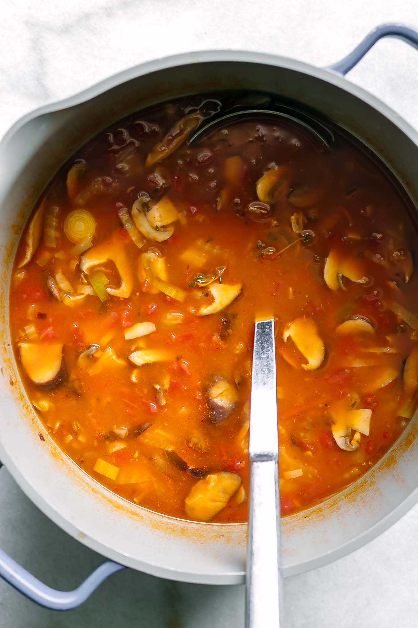 a pot of mushroom cioppino soup with a metal ladle on a white table