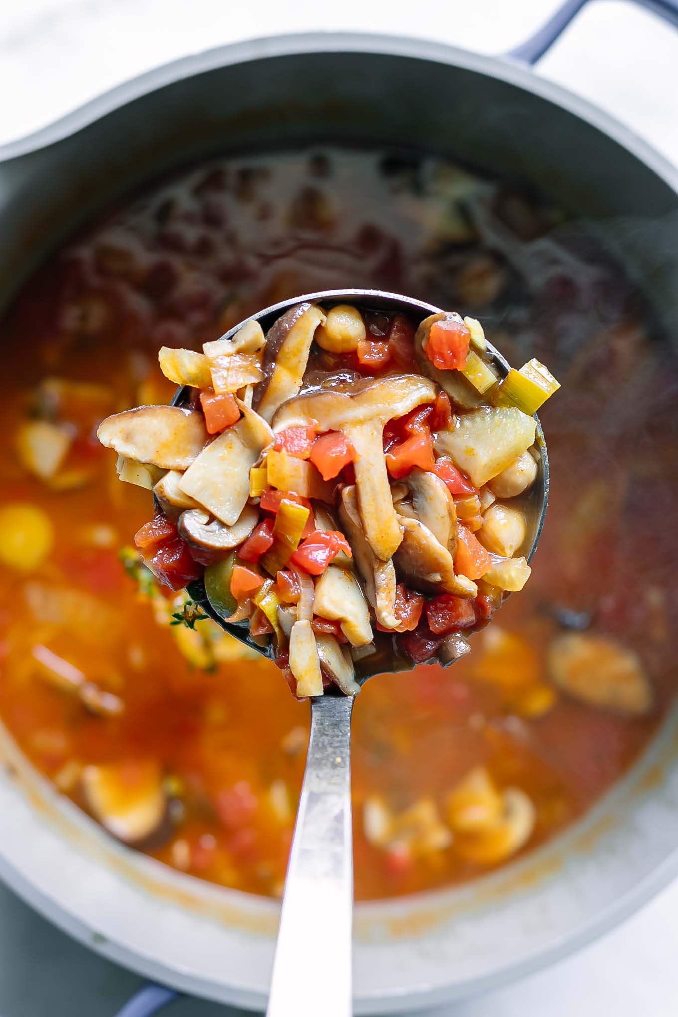 a ladle serving a mushroom cioppino soup over a large pot