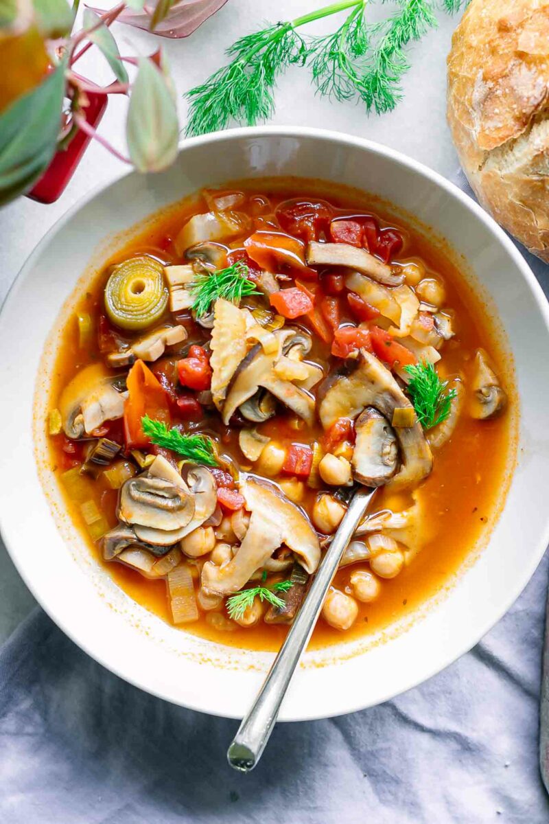 a white bowl with mushroom cioppino soup on a table with sourdough bread