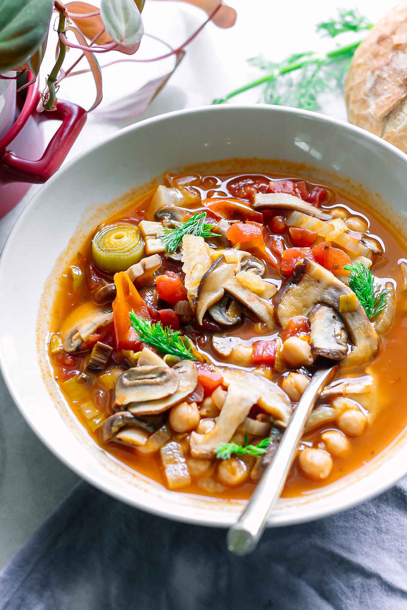 a bowl of mushroom cioppino soup on a white table with a gold fork