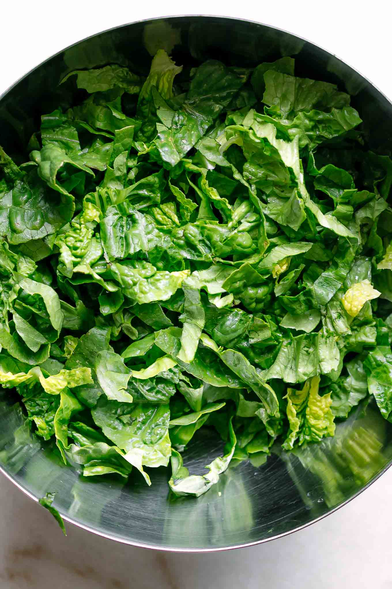 washed and cut romaine lettuce in a metal mixing bowl on a white table