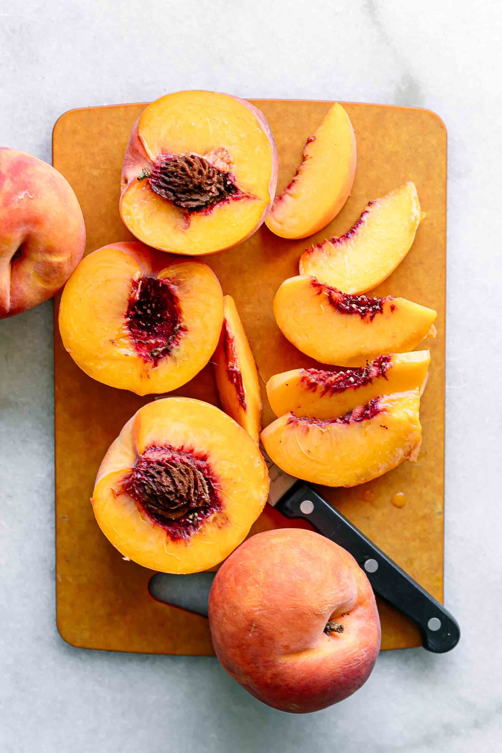 sliced and halved peaches on a wood cutting board with a knife